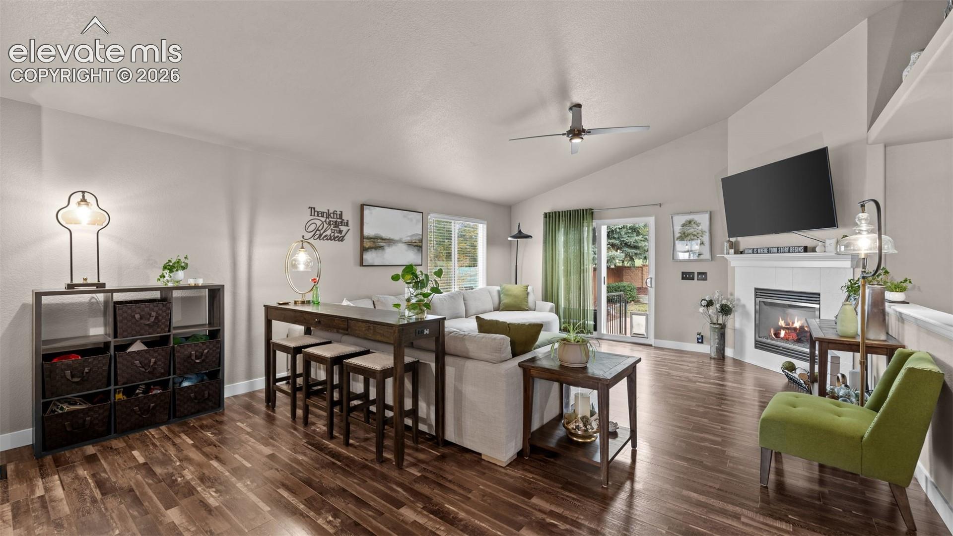 Vaulted ceilings, wood-finish flooring, white fireplace mantel, sliding glass door, and ceiling fan