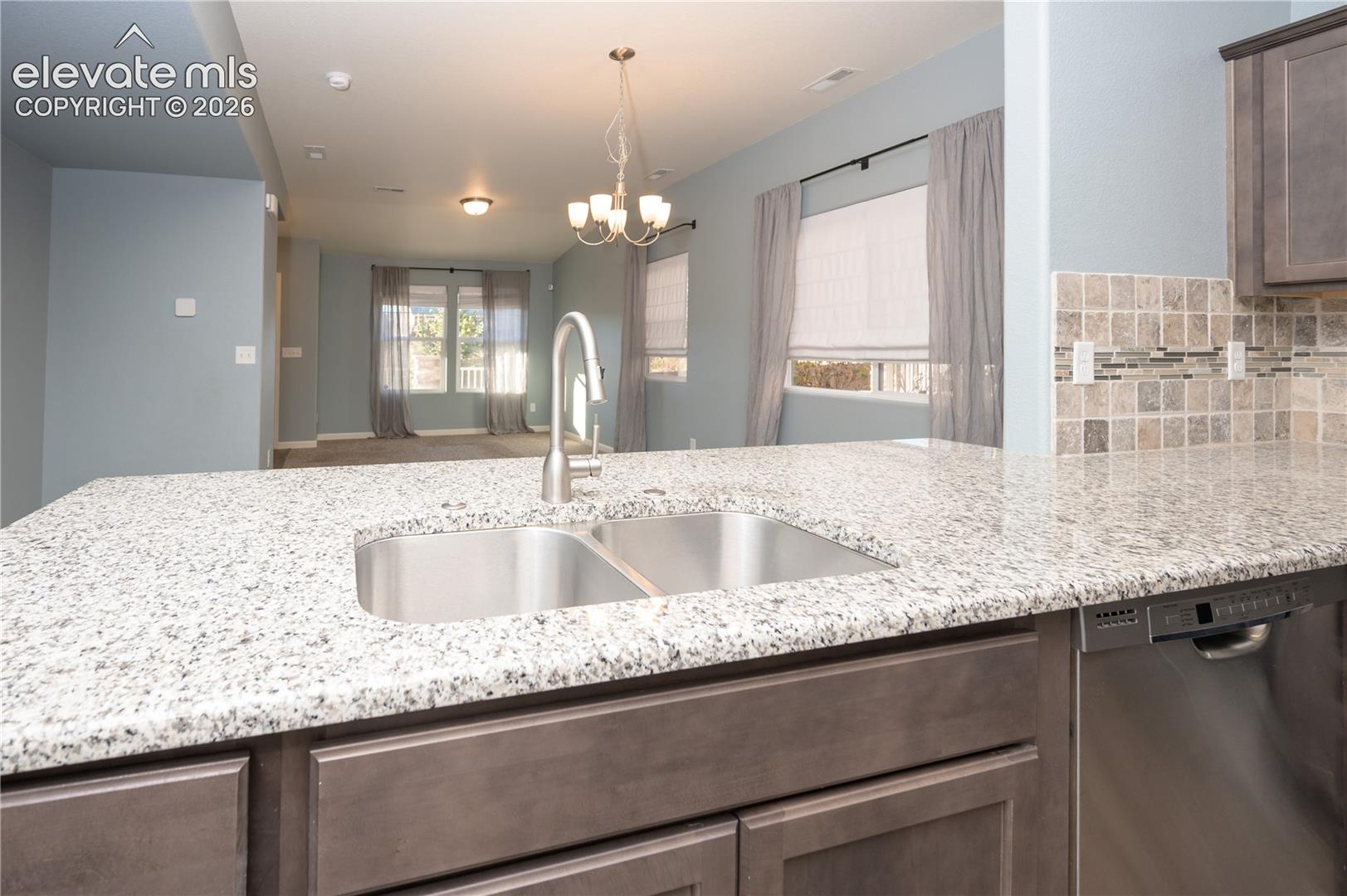 Kitchen featuring a stone countertop, dual-basin stainless steel sink with a pull-down faucet, tile backsplash, and stainless steel dishwasher