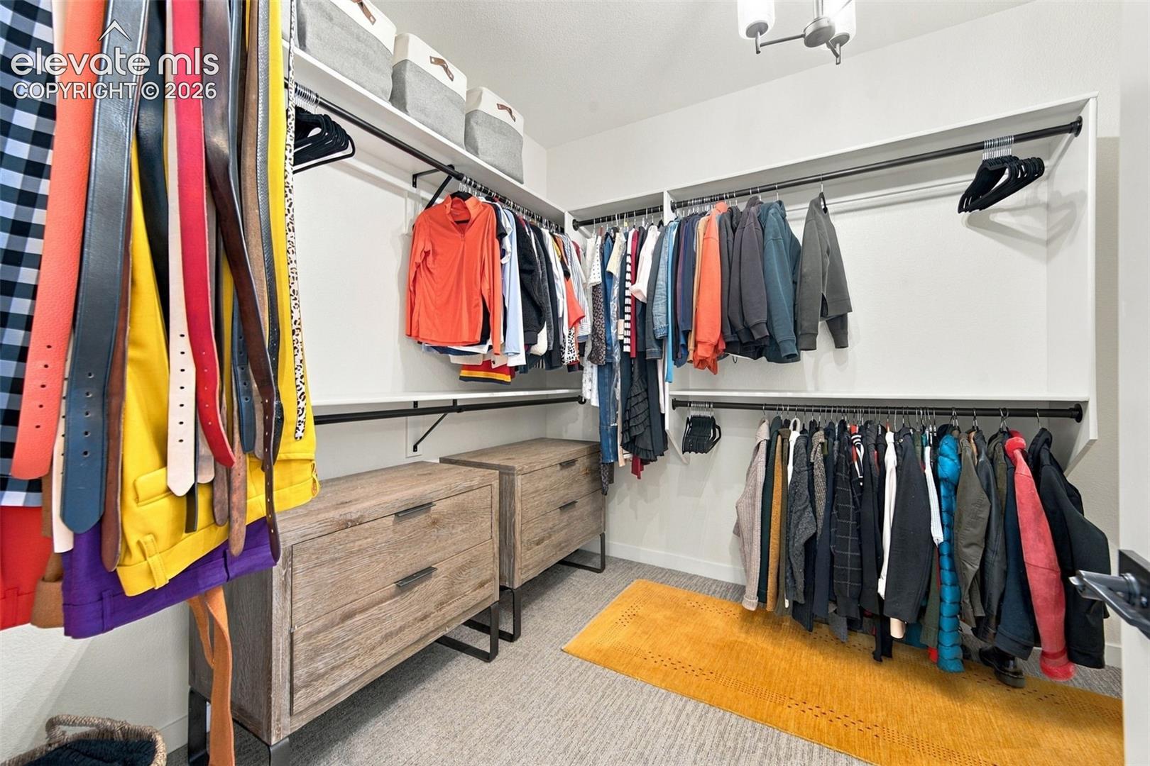 Walk-in closet featuring multi-level metal hanging rods, built-in white shelving, and two wood-finish cabinets with integrated hardware