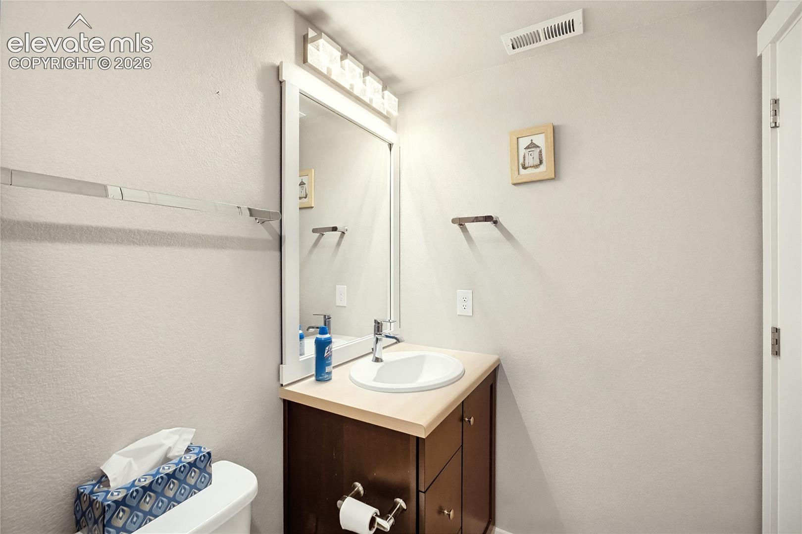 Dark wood vanity featuring a light-toned countertop, integrated white oval sink, chrome faucet, framed mirror, and mounted multi-bulb vanity light