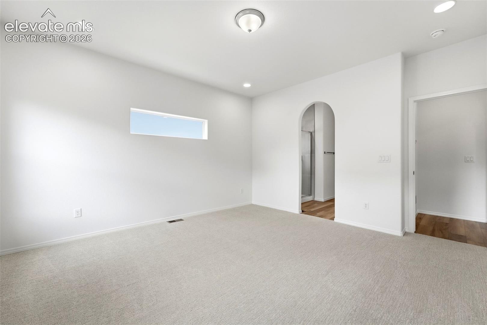 Interior space featuring neutral wall-to-wall carpeting, recessed ceiling lighting, a horizontal clerestory window, and an arched entryway