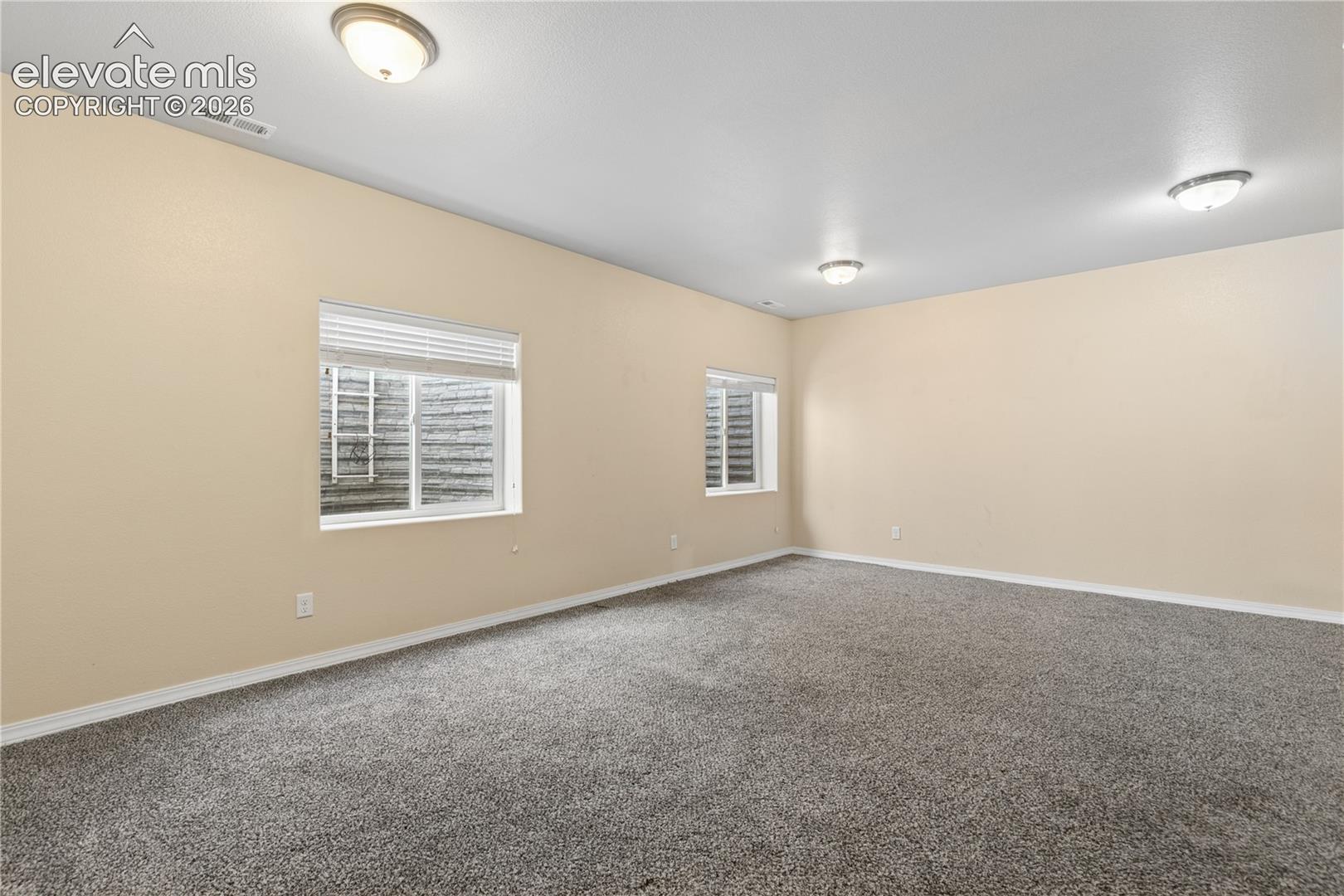 Expansive room featuring neutral wall tones, gray carpeting, and multiple ceiling-mounted light fixtures