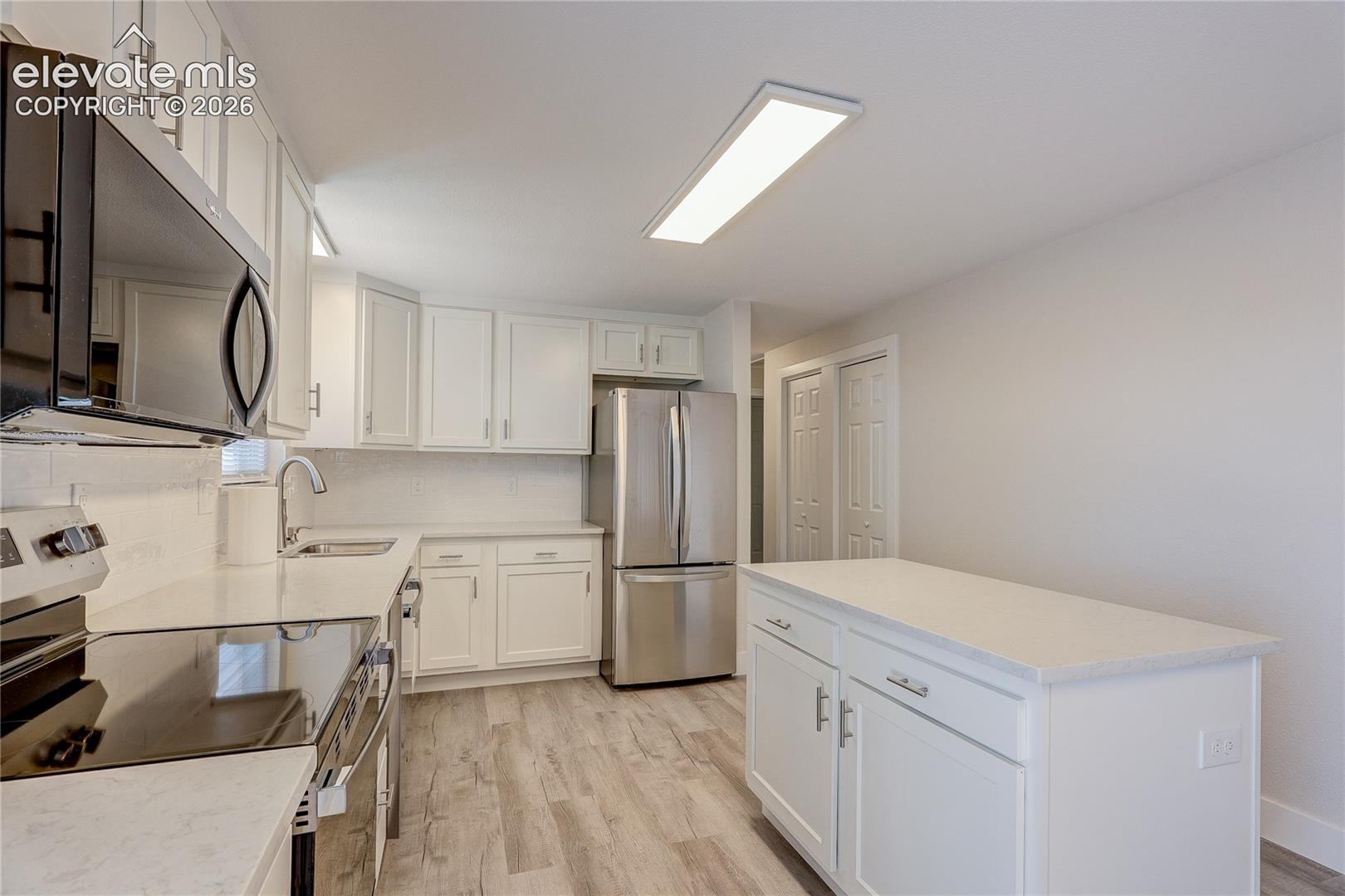 Kitchen featuring white shaker-style cabinetry, stainless steel appliances, quartz countertops, a central island, and wood-finish flooring