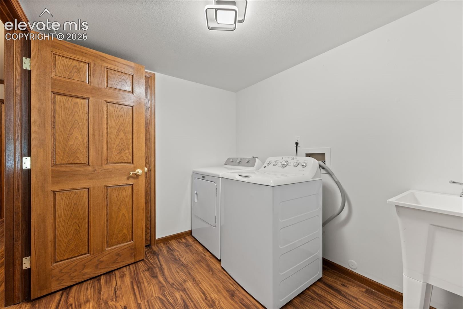 Dedicated laundry room featuring wood-finish flooring, white walls, and a utility sink
