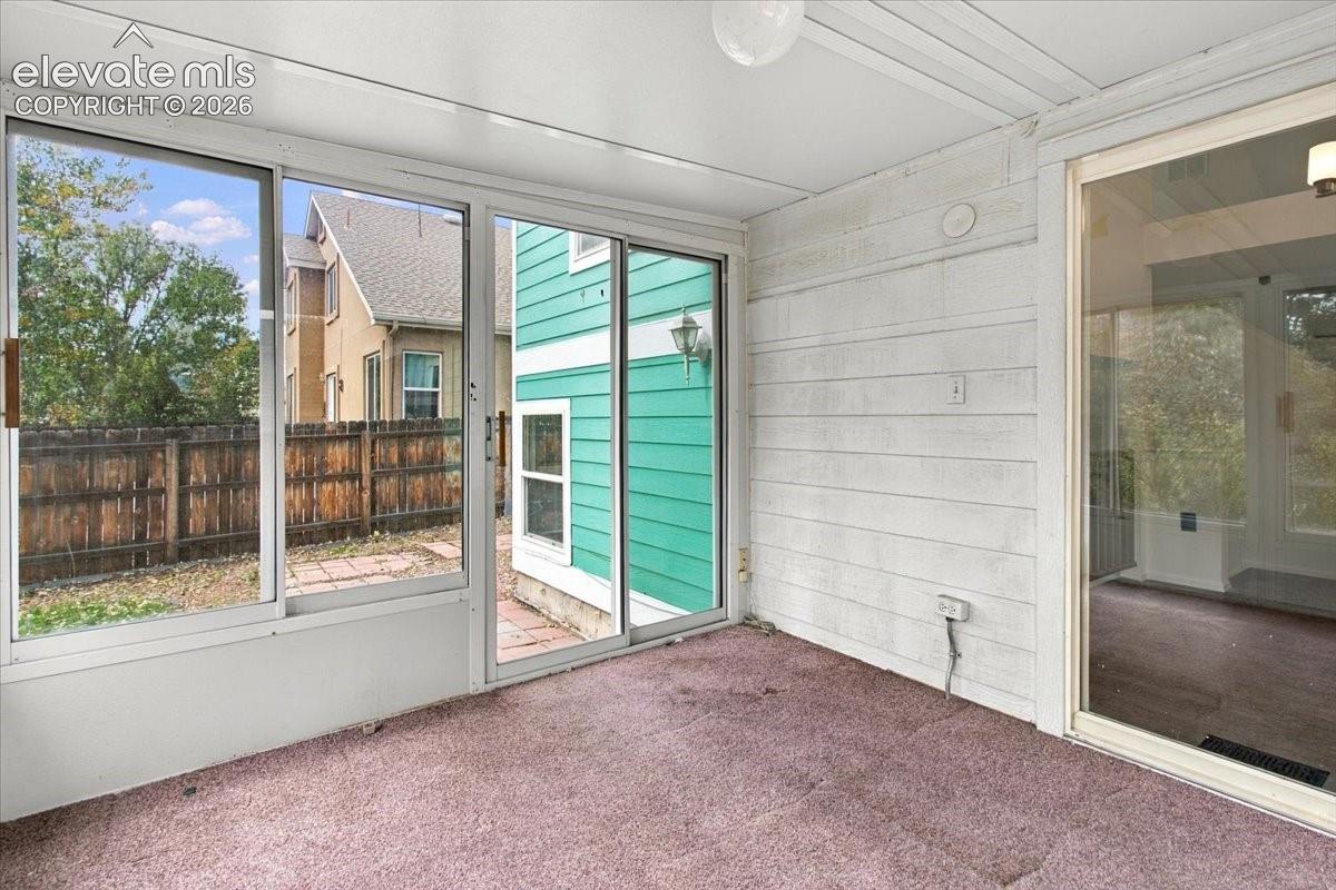 Enclosed sunroom featuring expansive sliding glass doors, white horizontal wall paneling, and a flush-mount ceiling light fixture