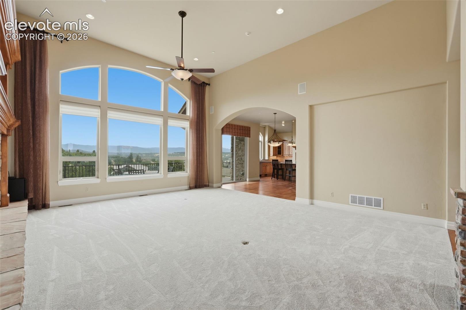 Spacious living area featuring expansive arched windows, high vaulted ceilings, recessed lighting, and light-toned carpeting