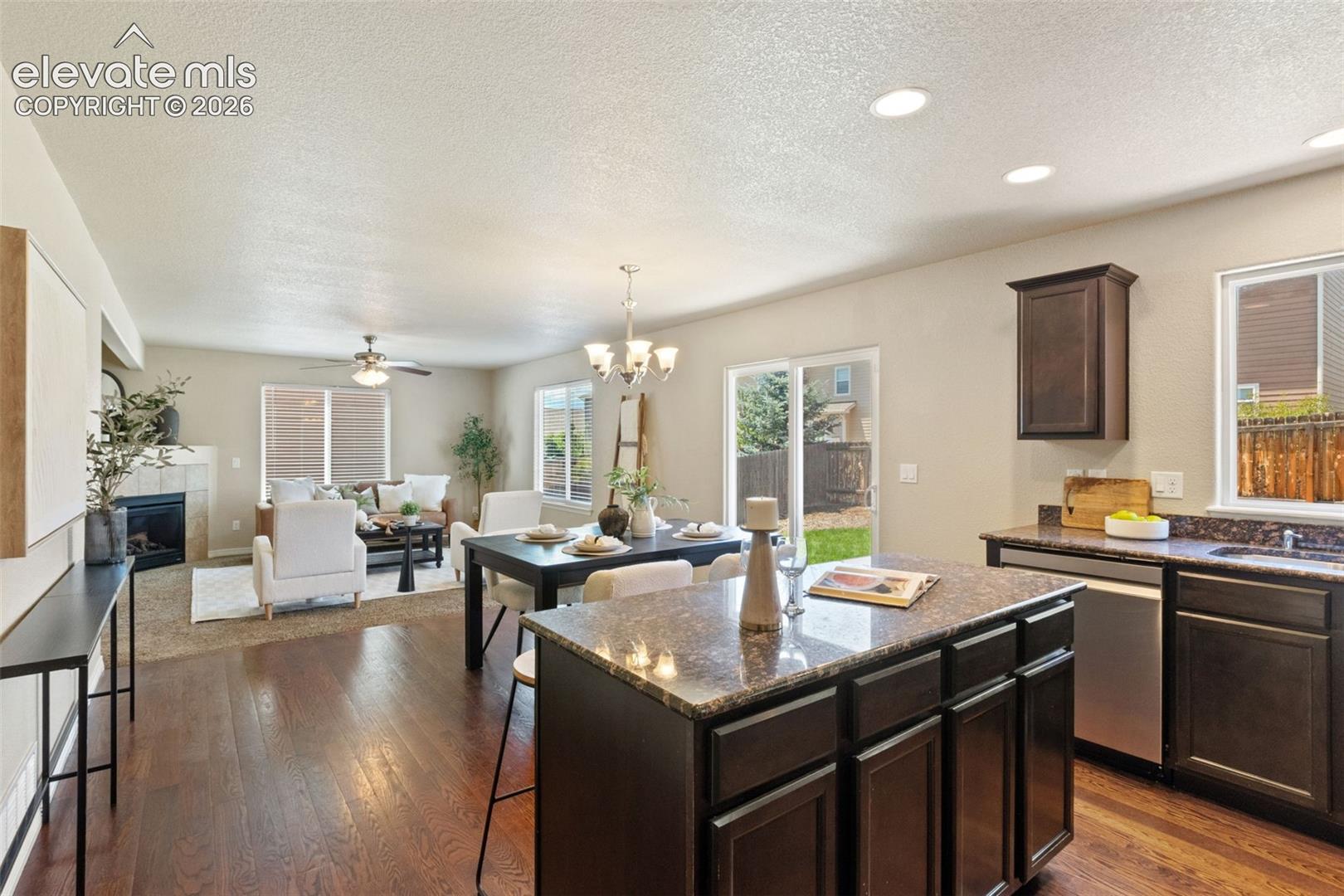 Open-concept living area featuring rich wood-finish flooring, a kitchen island with a dark granite countertop, dark wood cabinetry, and stainless steel appliances