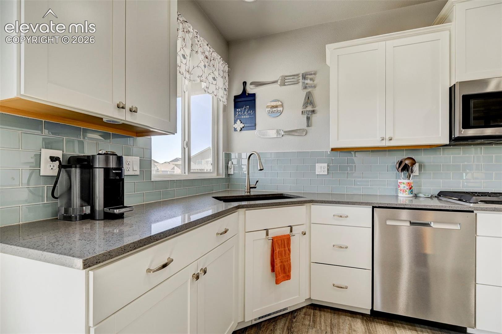 Kitchen featuring white cabinetry, grey speckled countertops, a light blue subway tile backsplash, stainless steel appliances, and a stainless steel sink with a gooseneck faucet