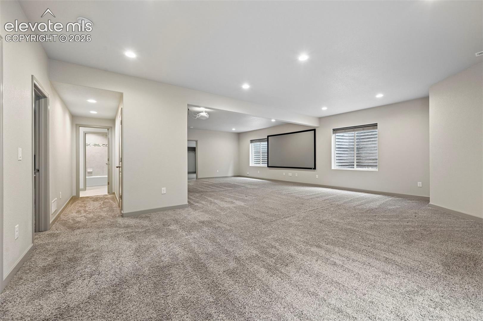 Open-concept room featuring neutral wall tones, recessed lighting, wall-to-wall carpeting, window wells, and a built-in projection screen