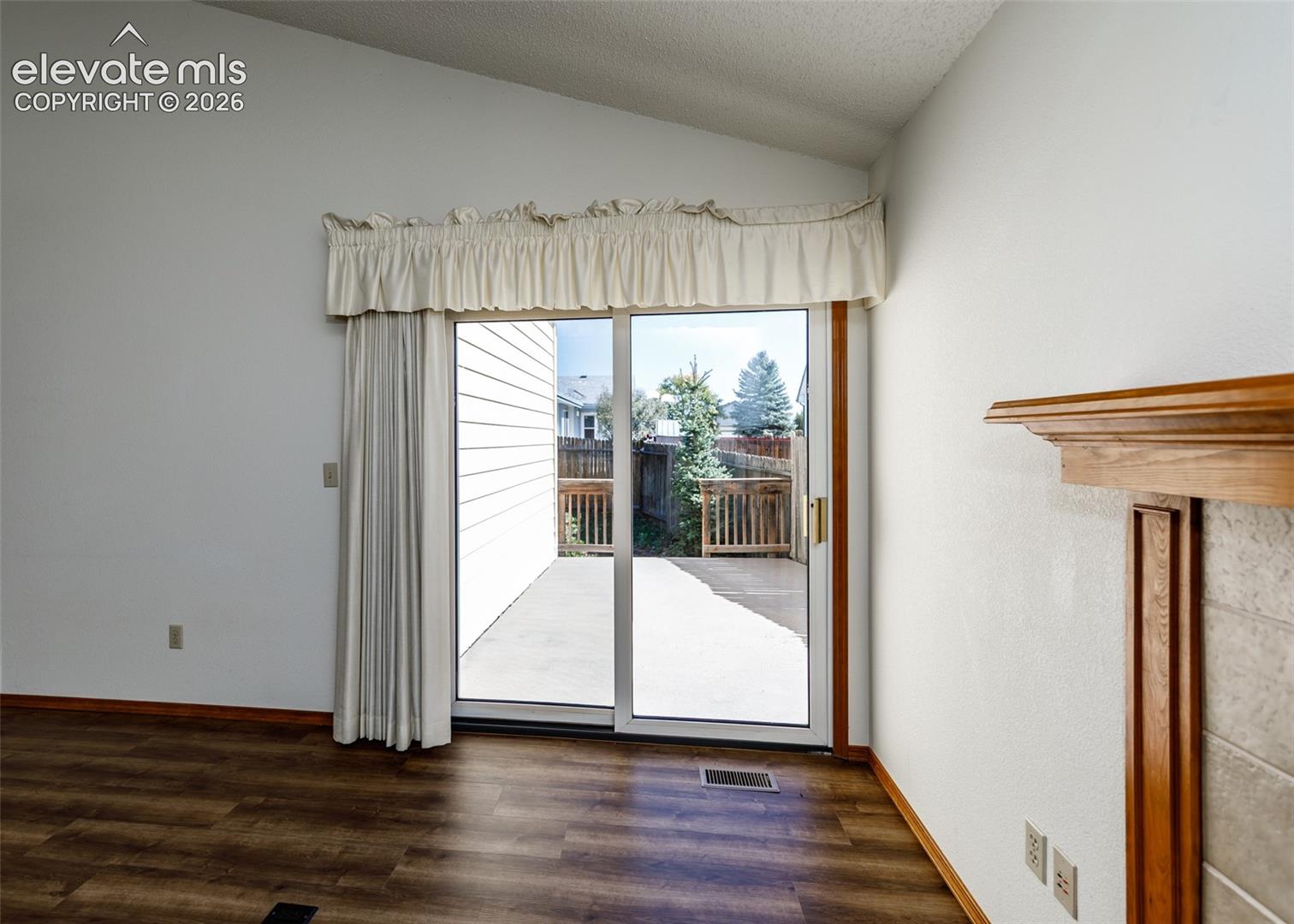 Vaulted ceiling, wood-finish flooring, sliding glass door, outdoor patio, and a wood mantel