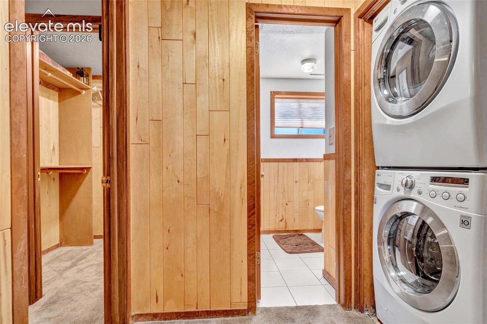 Utility area featuring a stacked washer and dryer, wood paneling, and white tile flooring