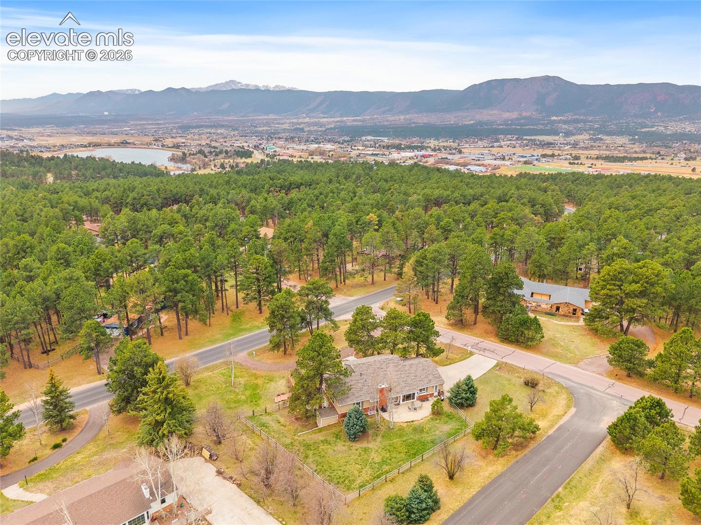Aerial perspective featuring expansive forested terrain, a paved driveway, and prominent mountain range backdrop