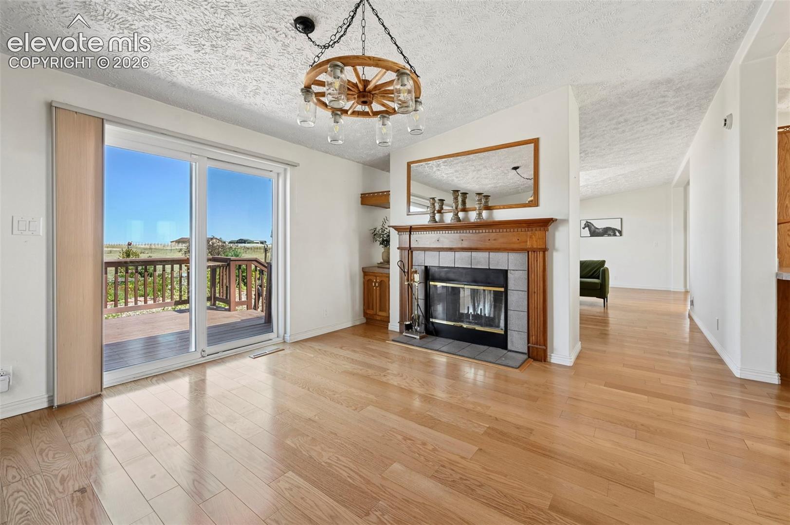 Hardwood-finish flooring, a fireplace with a wood mantel and tile surround, and sliding glass doors opening to an exterior deck