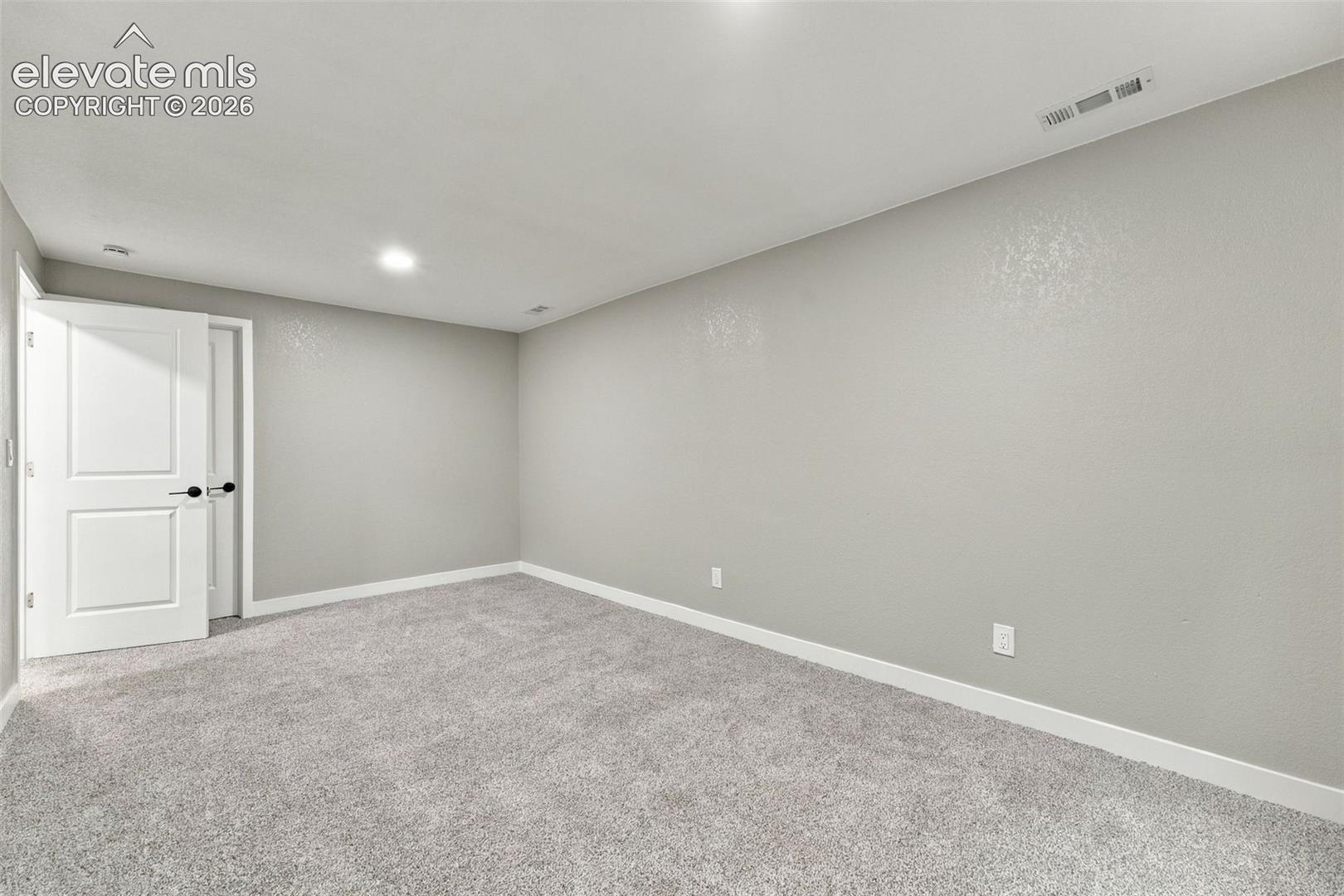 Neutral-toned wall paint, recessed lighting, and high-pile wall-to-wall carpeting complemented by a solid core two-panel interior door with matte black hardware