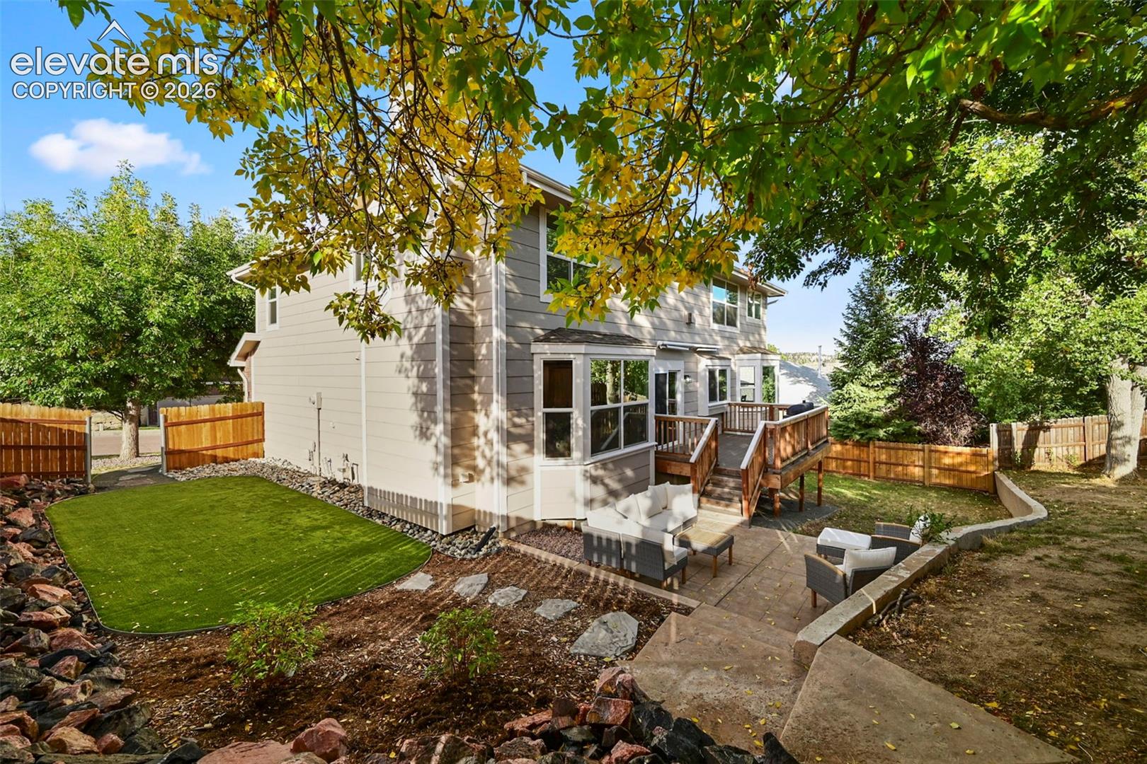 Expansive rear exterior featuring a multi-level wood deck, concrete patio, and a fenced yard with artificial turf