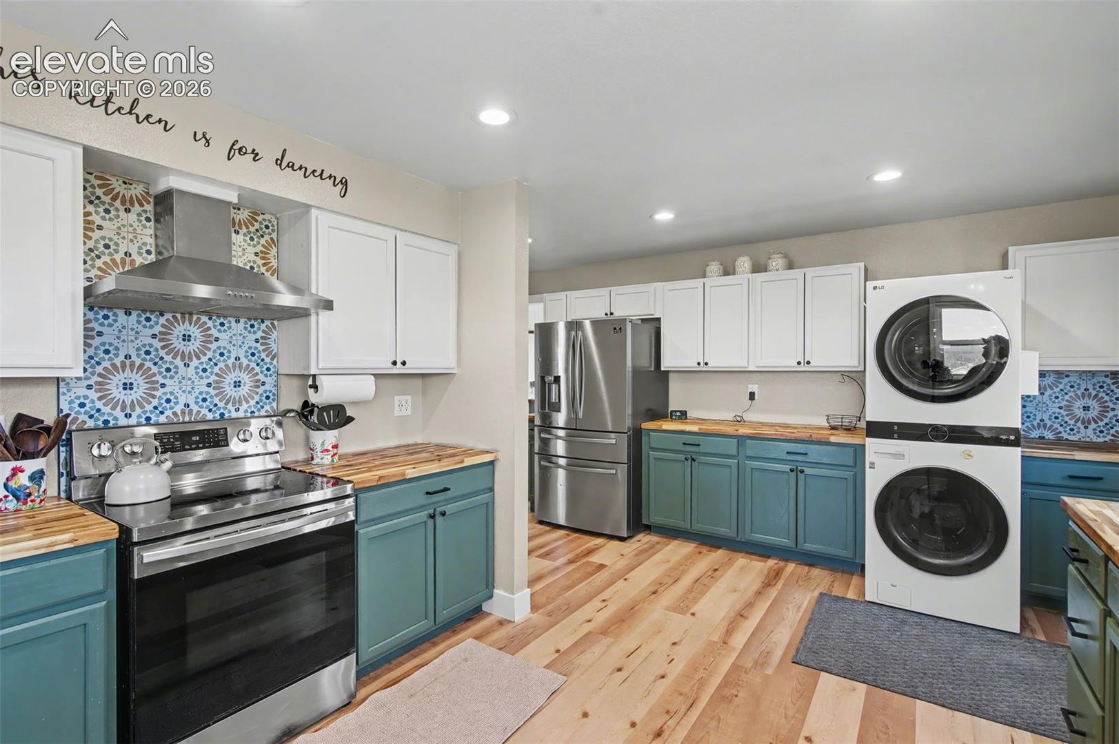 Kitchen featuring two-tone cabinetry, wood-finish countertops, patterned tile backsplash, stainless steel appliances, and wood-finish flooring