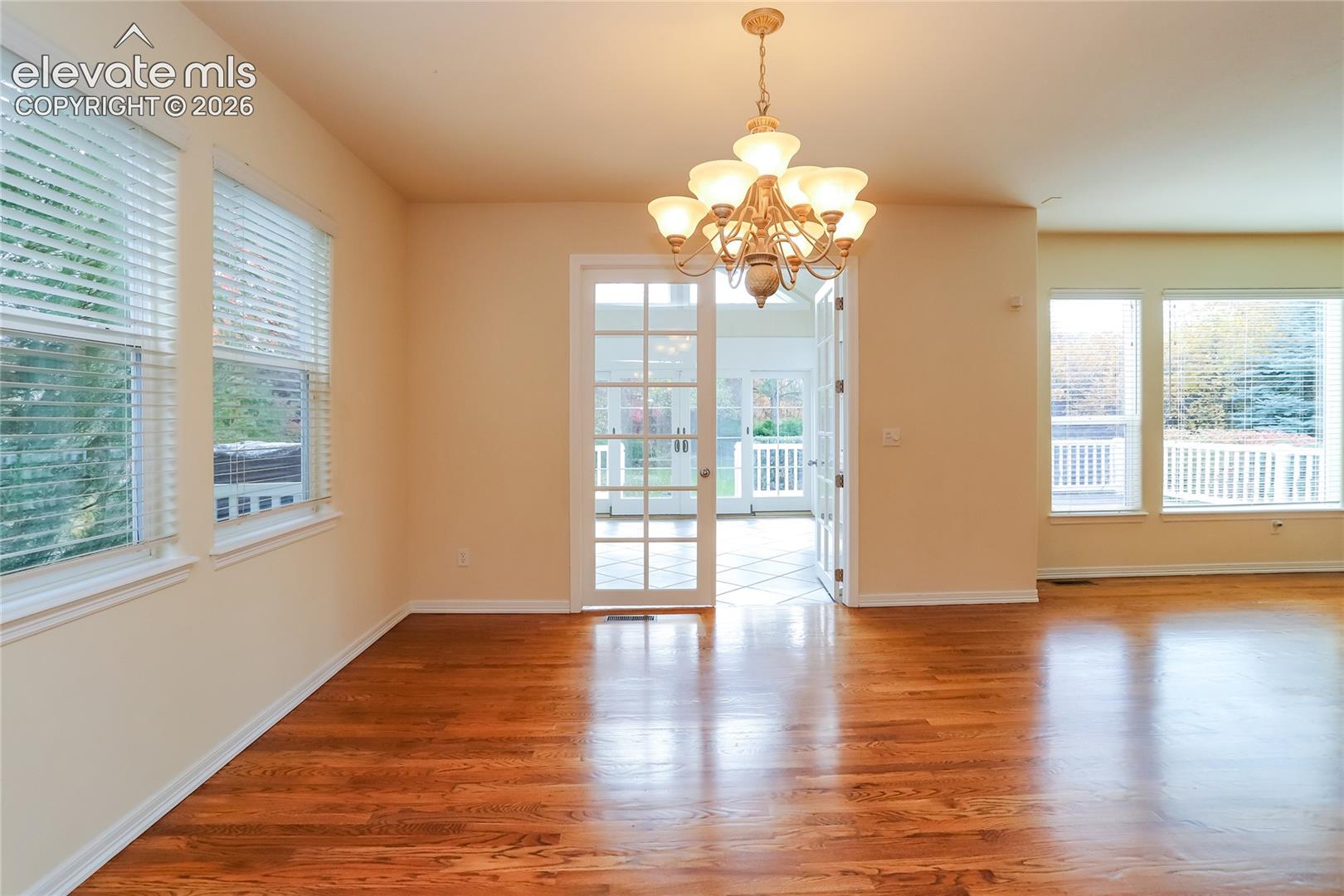 Hardwood flooring, multi-pane glass French doors, multi-pane windows, and a multi-arm chandelier