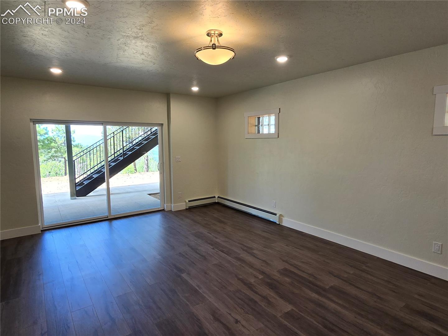 Lower level bedroom featuring a baseboard heating unit, dark wood-type flooring, and a textured ceiling