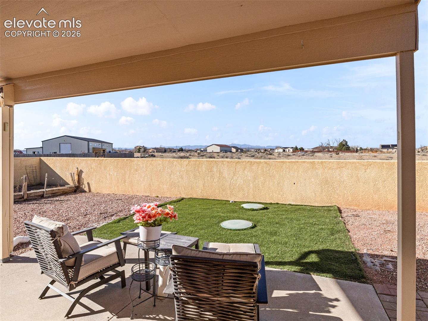 Covered patio with concrete flooring, low perimeter wall, and a grass area