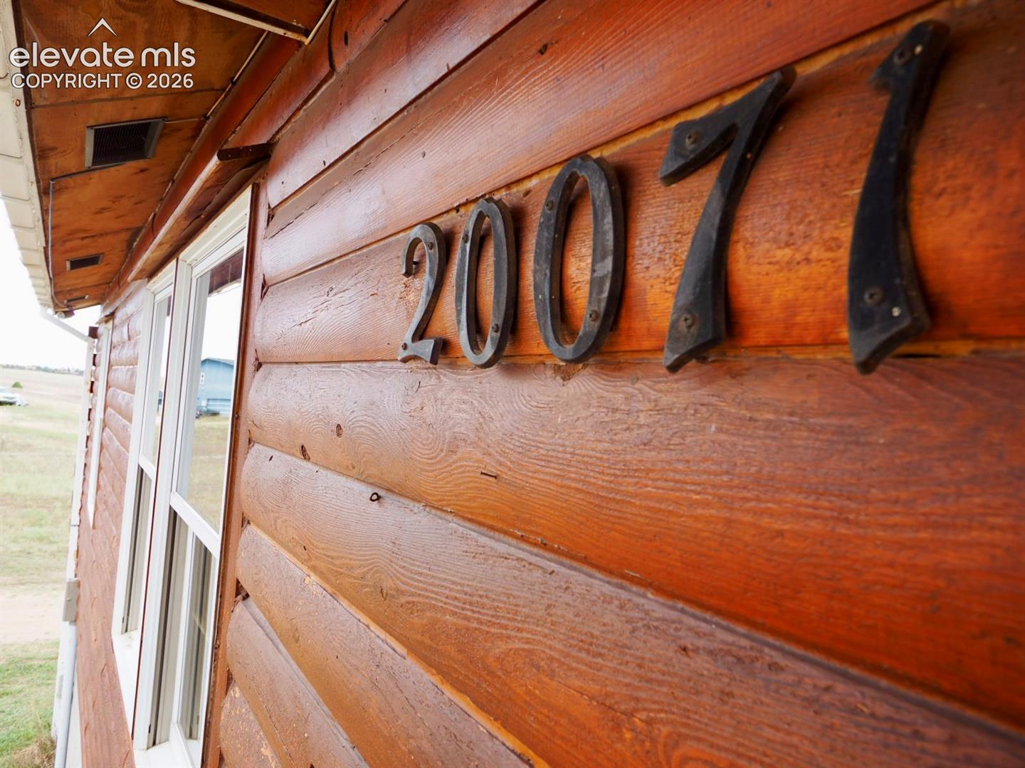 Exterior facade featuring horizontal log siding, metal house numerals, and white-framed windows