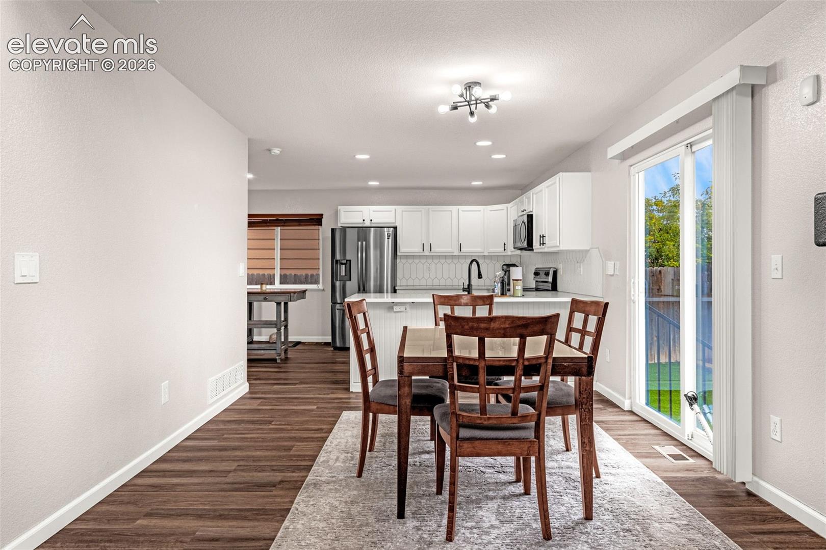 Kitchen featuring white shaker-style cabinetry, stainless steel appliances, and a peninsula, complemented by wood-finish flooring and a sliding glass door