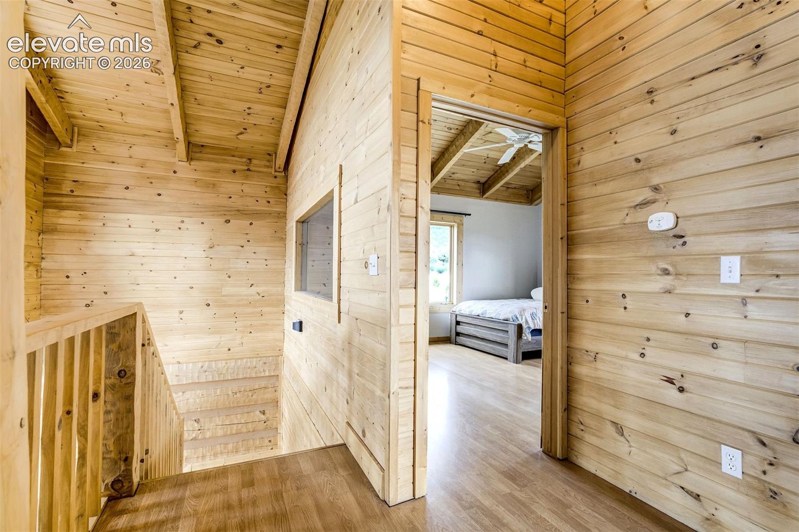 Wood-paneled hallway featuring a wood-finish flooring, staircase with wood railing, and an interior window