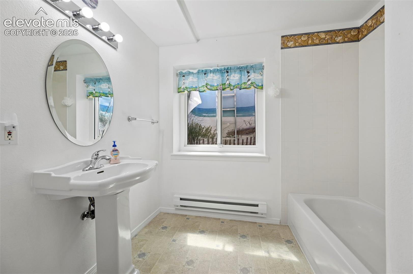 Pedestal sink with chrome faucet, oval mirror, wall-mounted vanity lighting, and built-in tub