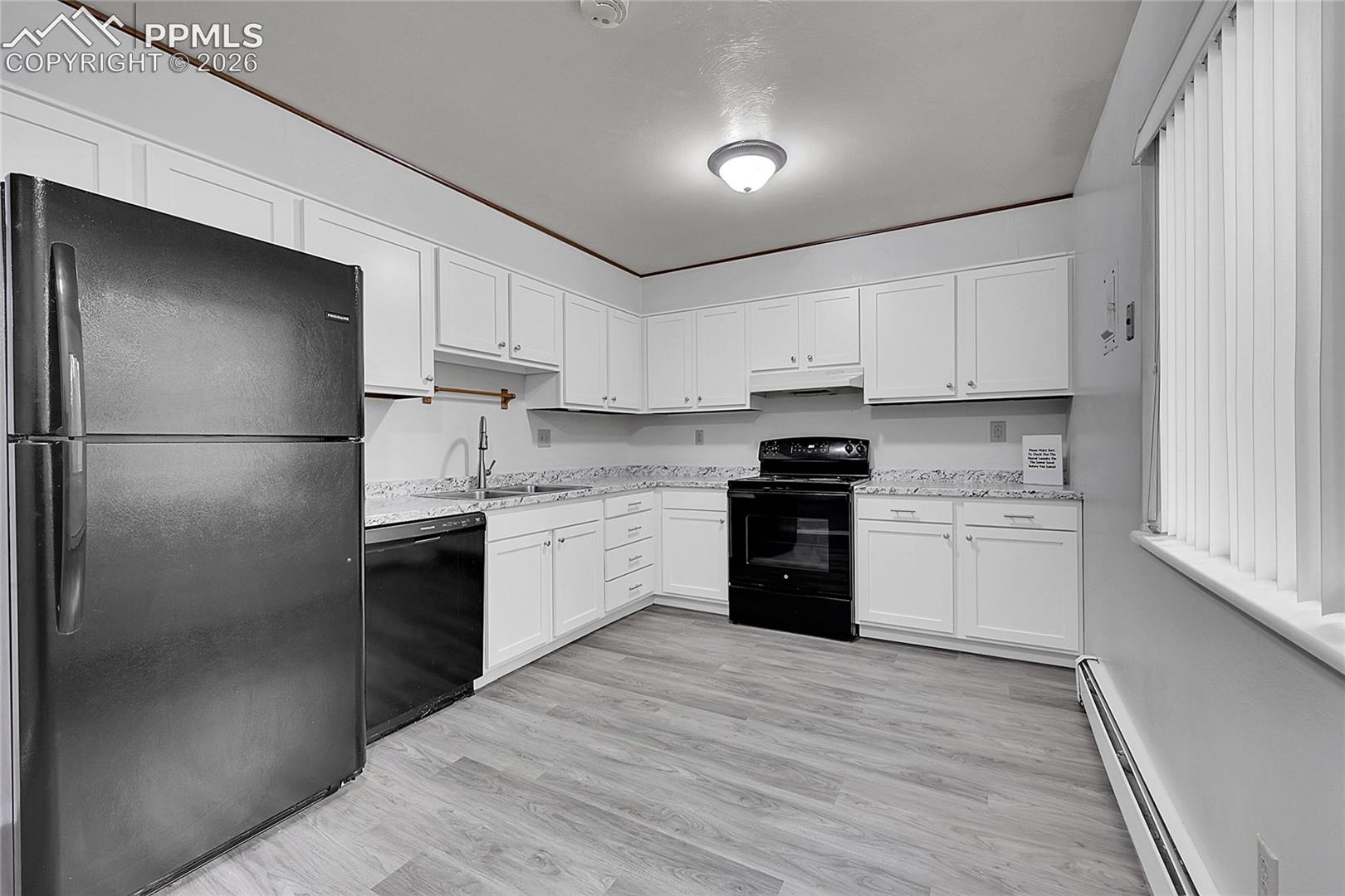 Kitchen featuring black appliances, a baseboard heating unit, white cabinets, light stone countertops, and light wood-style flooring
