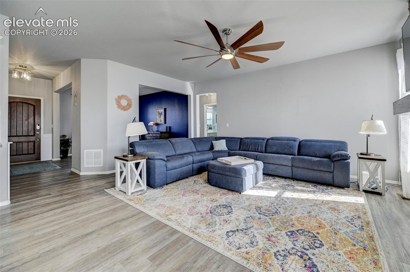 Spacious living area featuring wood-finish flooring, a contemporary ceiling fan, and abundant natural light