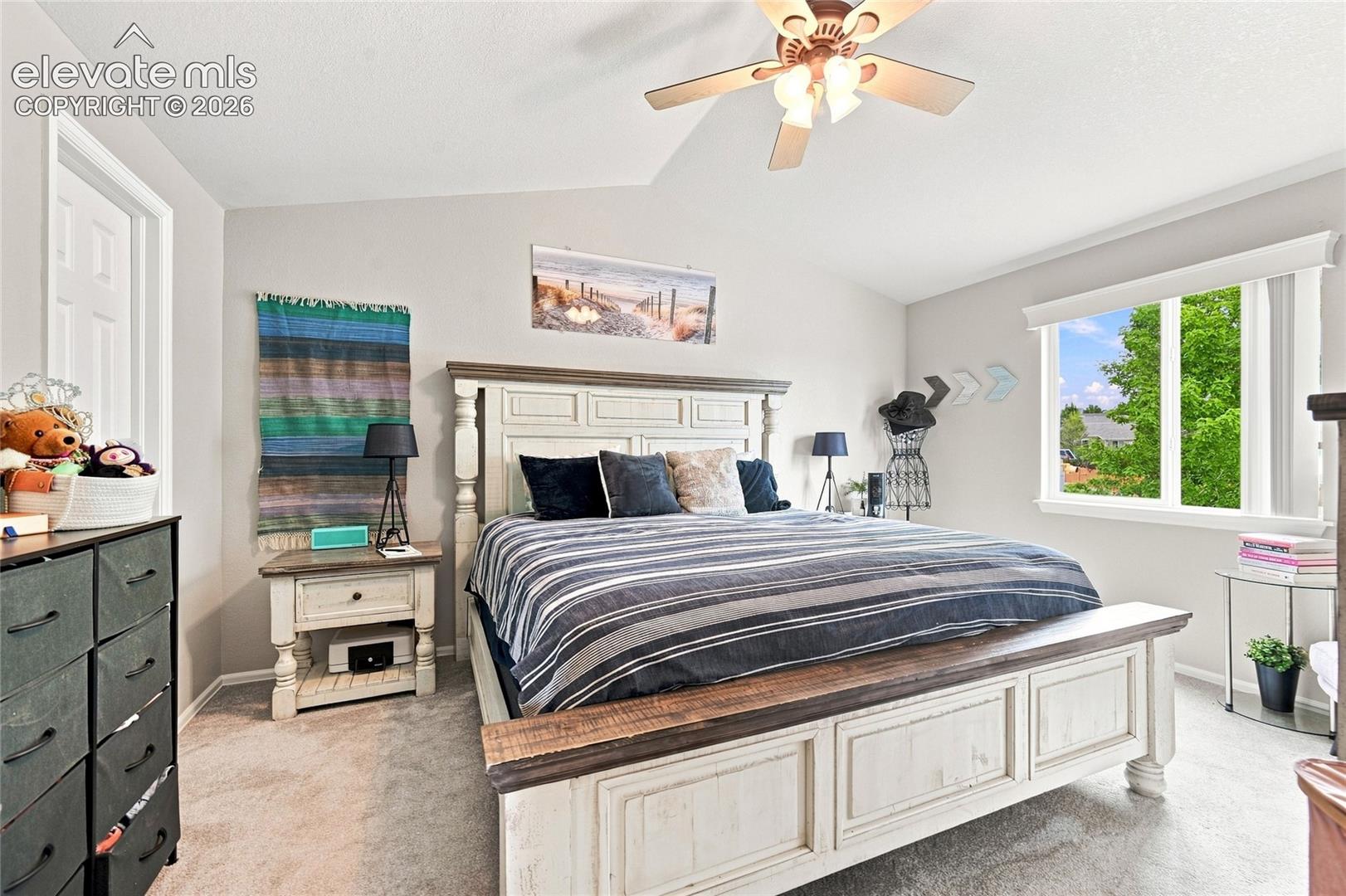 Vaulted ceilings, neutral wall tones, wall-to-wall carpeting, multi-pane window, and a ceiling fan with integrated lighting