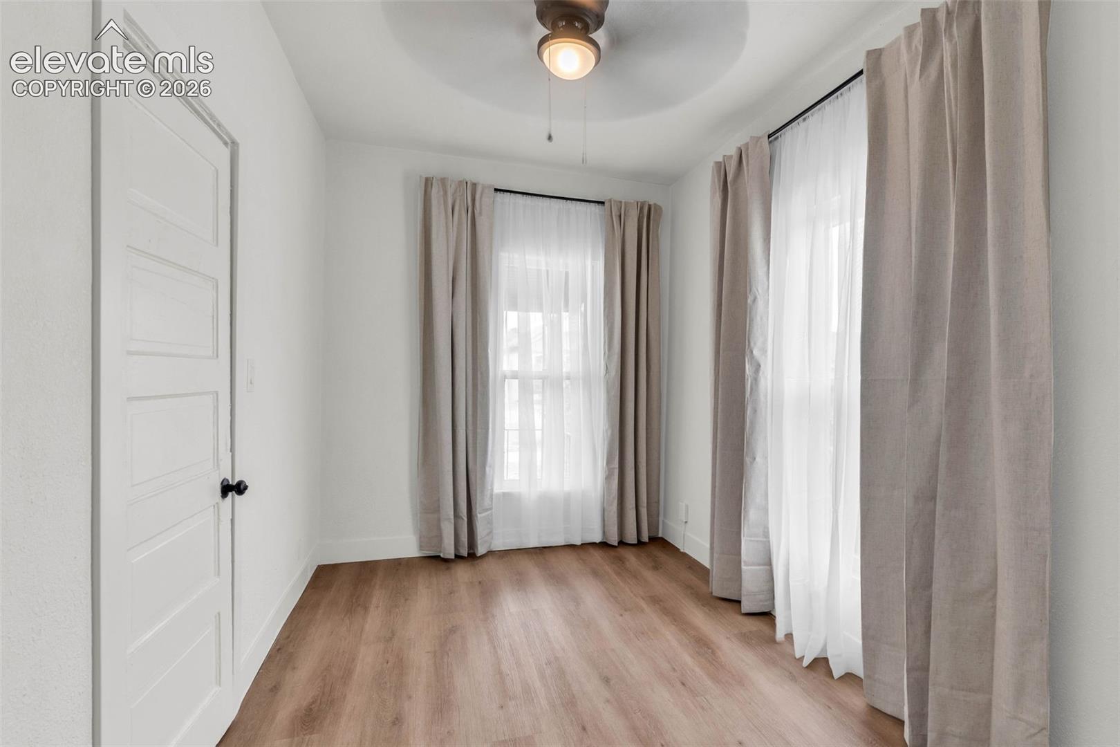 Wood-finish flooring, white four-panel interior door, and ceiling fan with integrated lighting fixture