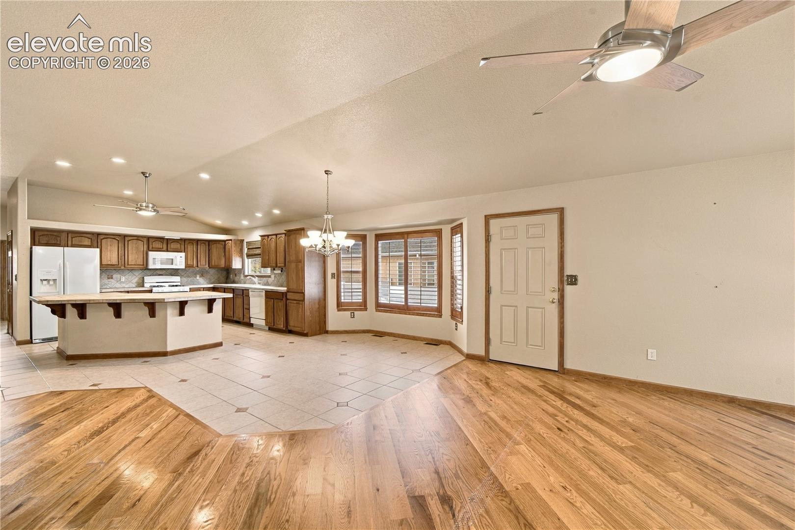 Kitchen featuring stained wood cabinetry, a breakfast bar, and tile flooring, paired with wood-finish flooring, ceiling fans, and a bay window