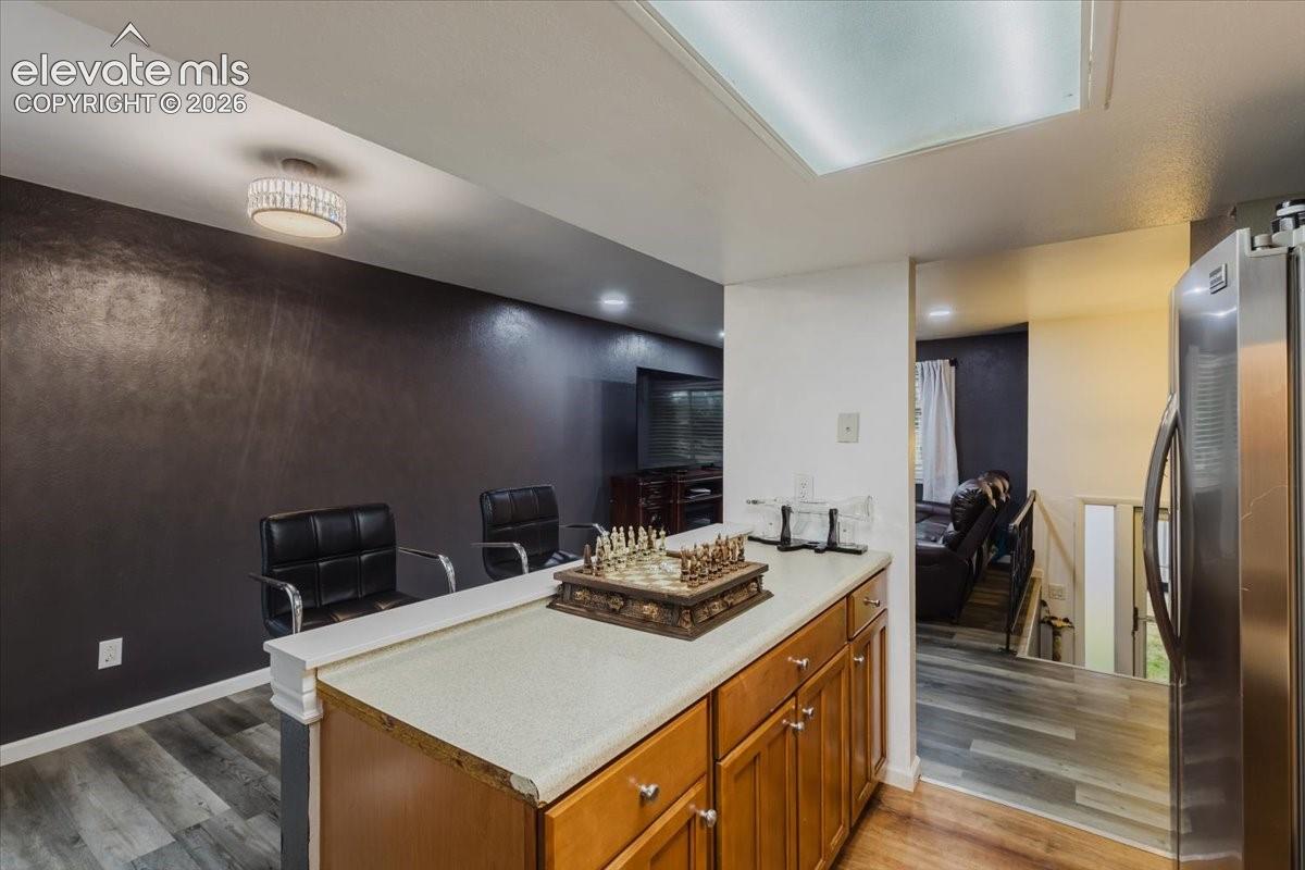 Kitchen counter with wood-finish cabinetry, light-toned countertop, and stainless steel refrigerator