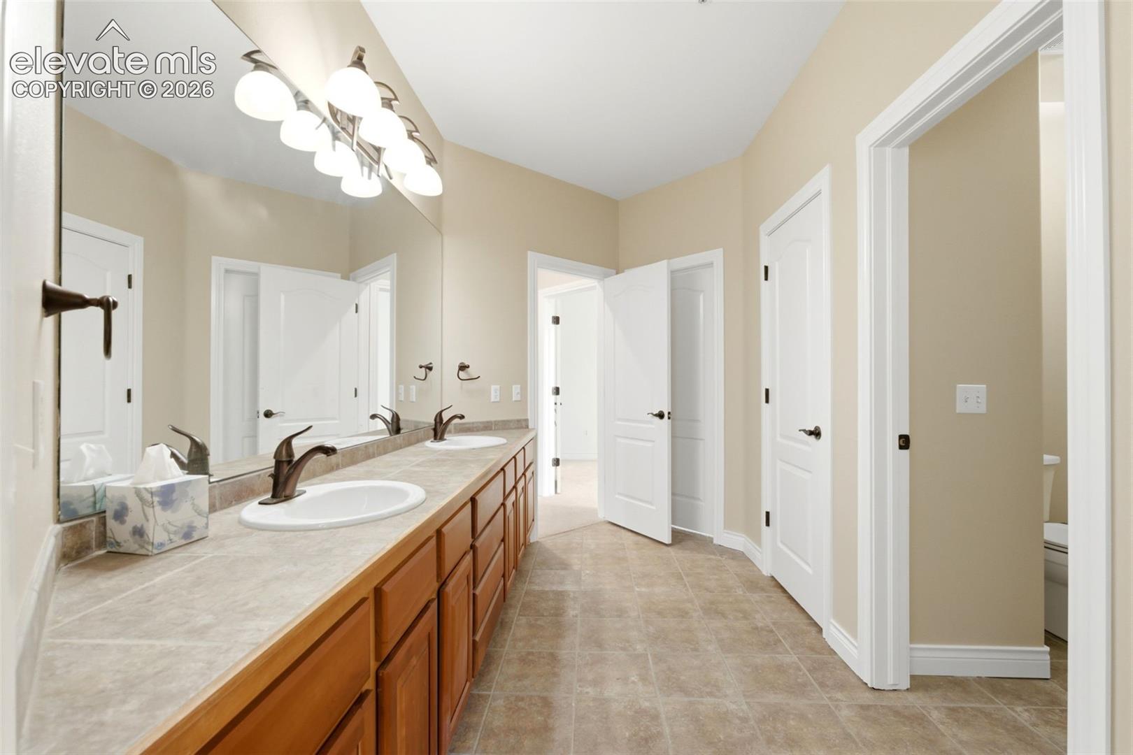 Dual vanity with wood-finish cabinetry, integrated sinks, bronze-finish faucets, and an expansive wall mirror