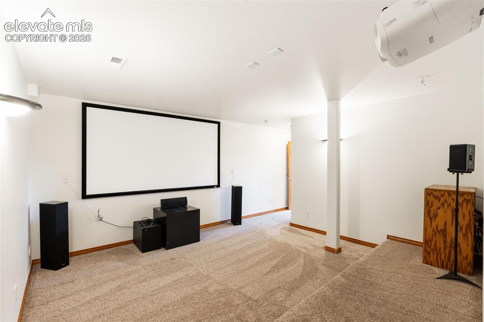 Multi-level room featuring wall-to-wall carpeting, a fixed-screen projection display, and a ceiling-mounted digital projector