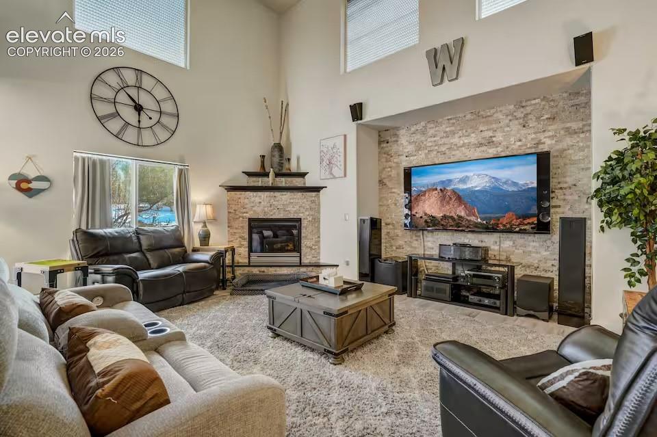 Spacious living area featuring a stone-clad fireplace with a dark wood mantle, high ceilings, large windows, and an entertainment wall with a stone accent