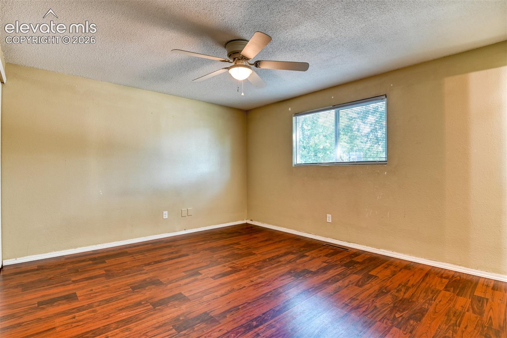 Spacious room featuring wood-finish flooring, a ceiling fan with integrated lighting, and a large window