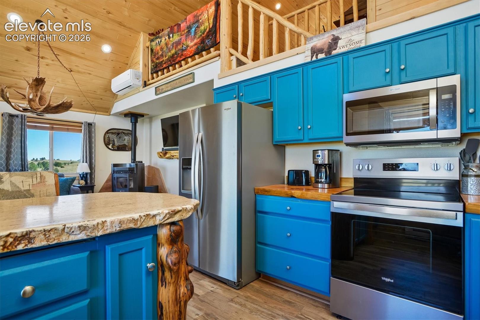 Kitchen featuring teal cabinetry, wood-finish countertops, and stainless steel appliances including a refrigerator, range, and microwave