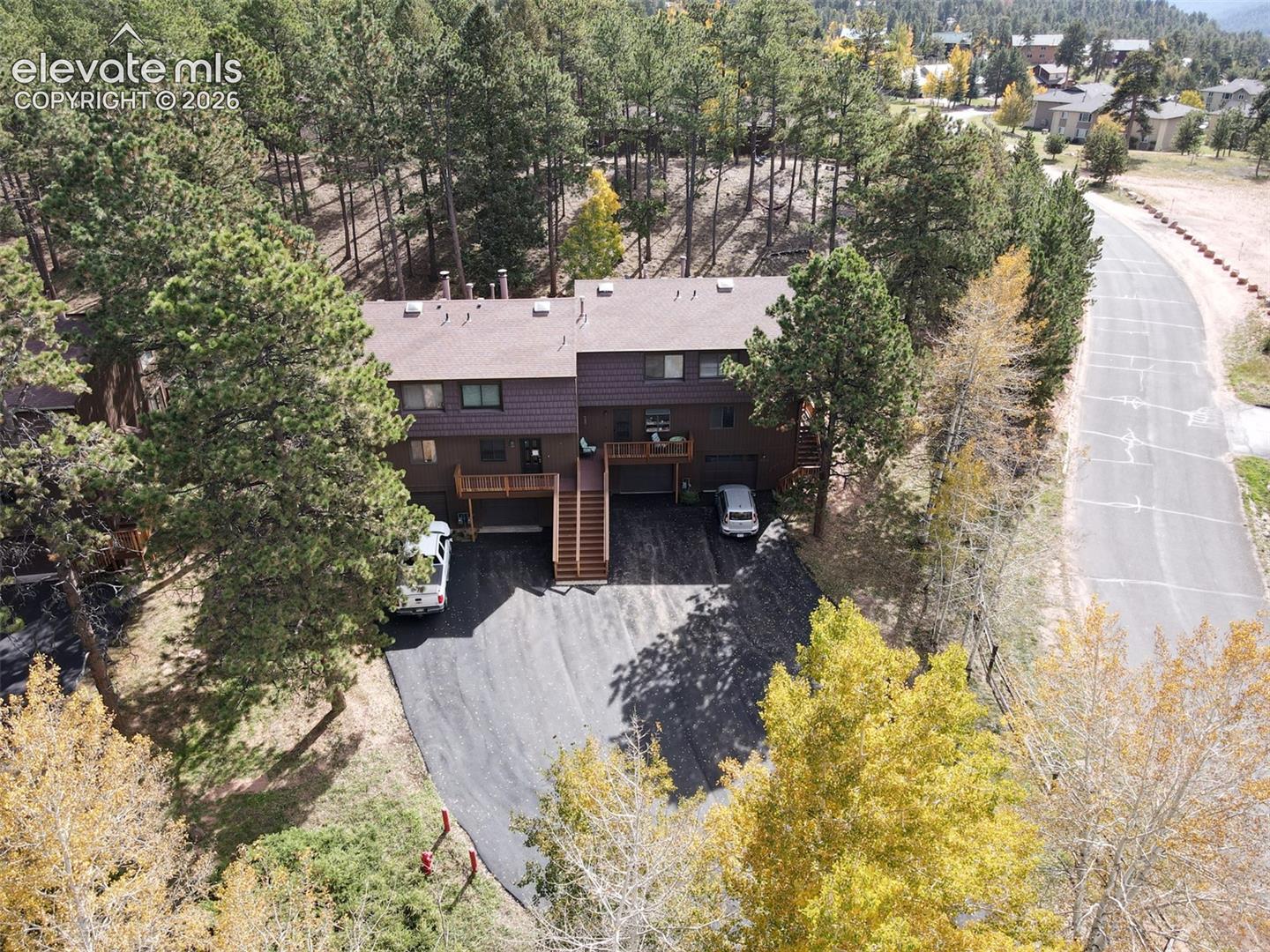 Duplex structure with brown siding and a dark shingle roof, surrounded by mature trees