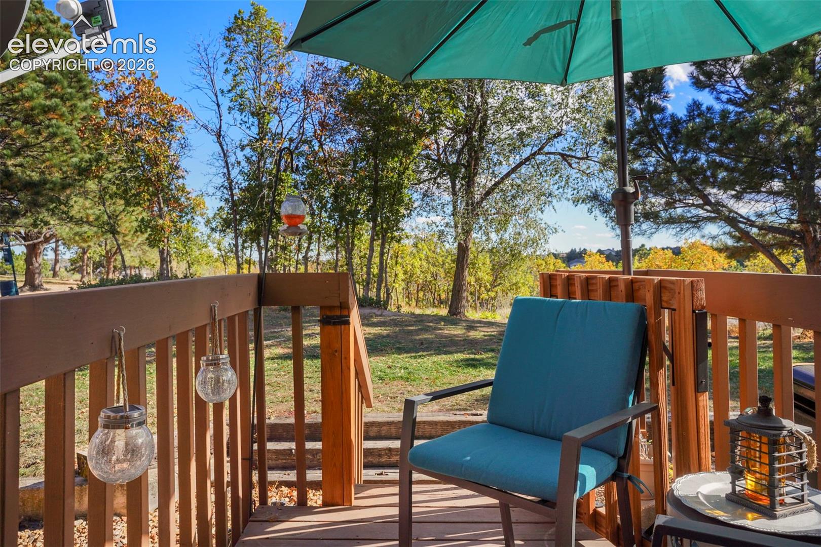 Elevated wooden deck featuring a perimeter railing, mature trees, and a natural landscape setting
