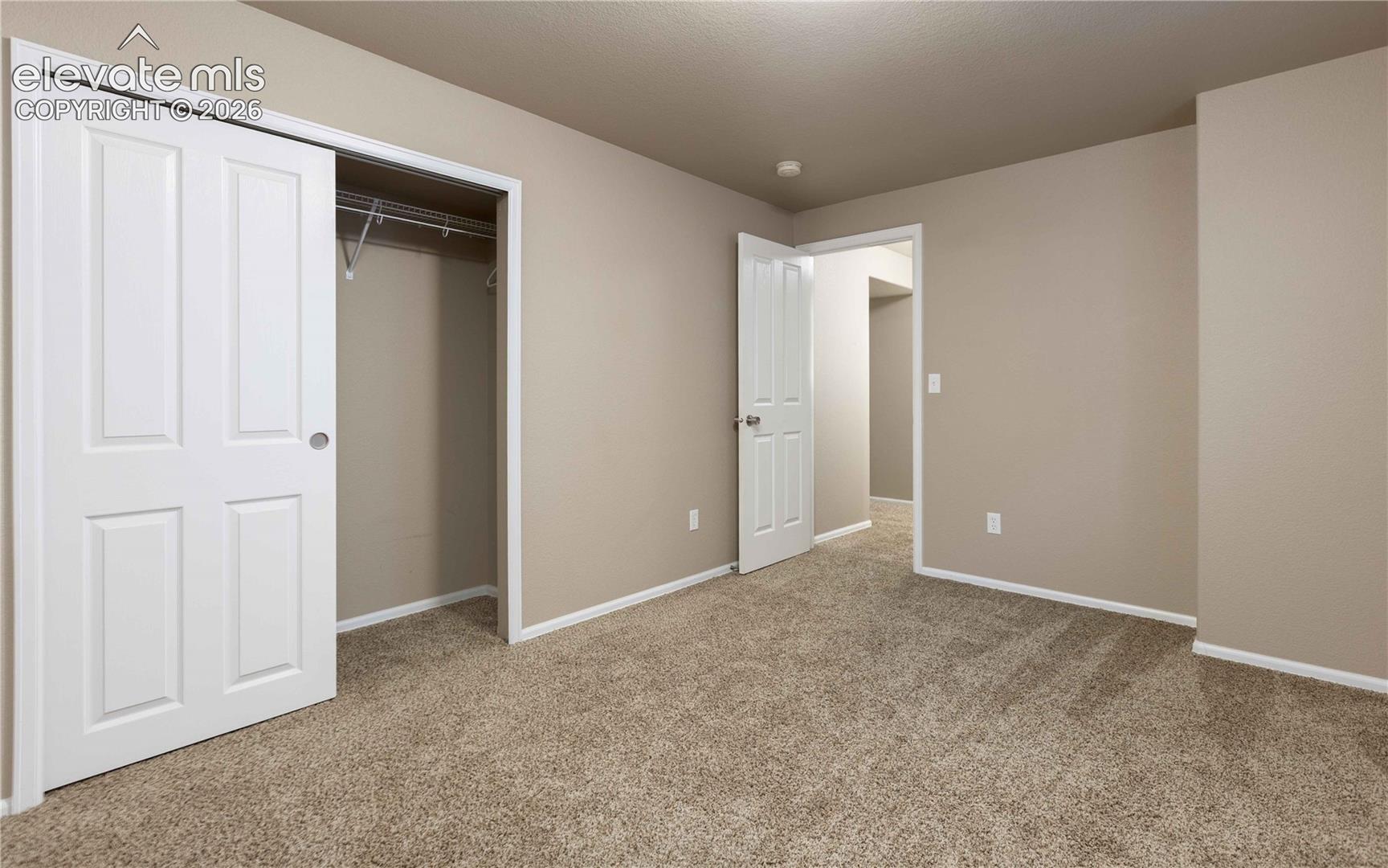 Neutral-toned interior space featuring neutral wall paint, wall-to-wall carpeting, a sliding panel closet door, and a six-panel door