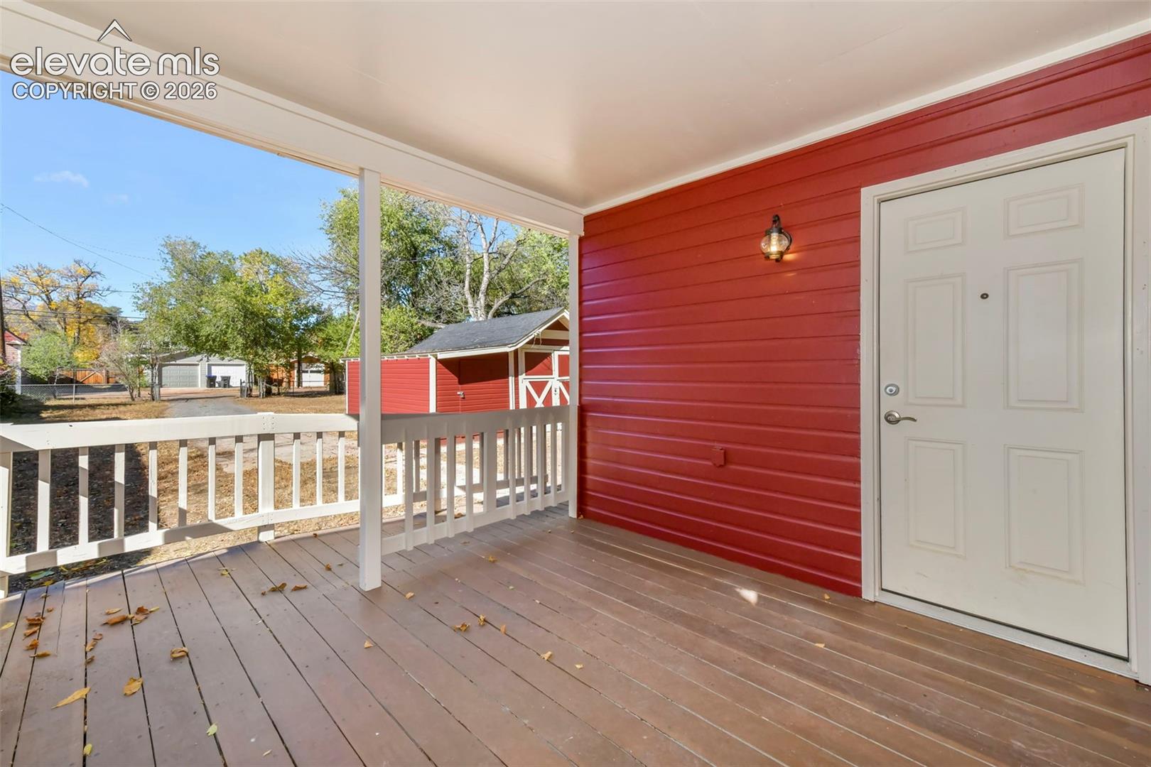 Covered wooden porch featuring horizontal red siding, white picket railing, and an exterior wall-mounted light fixture