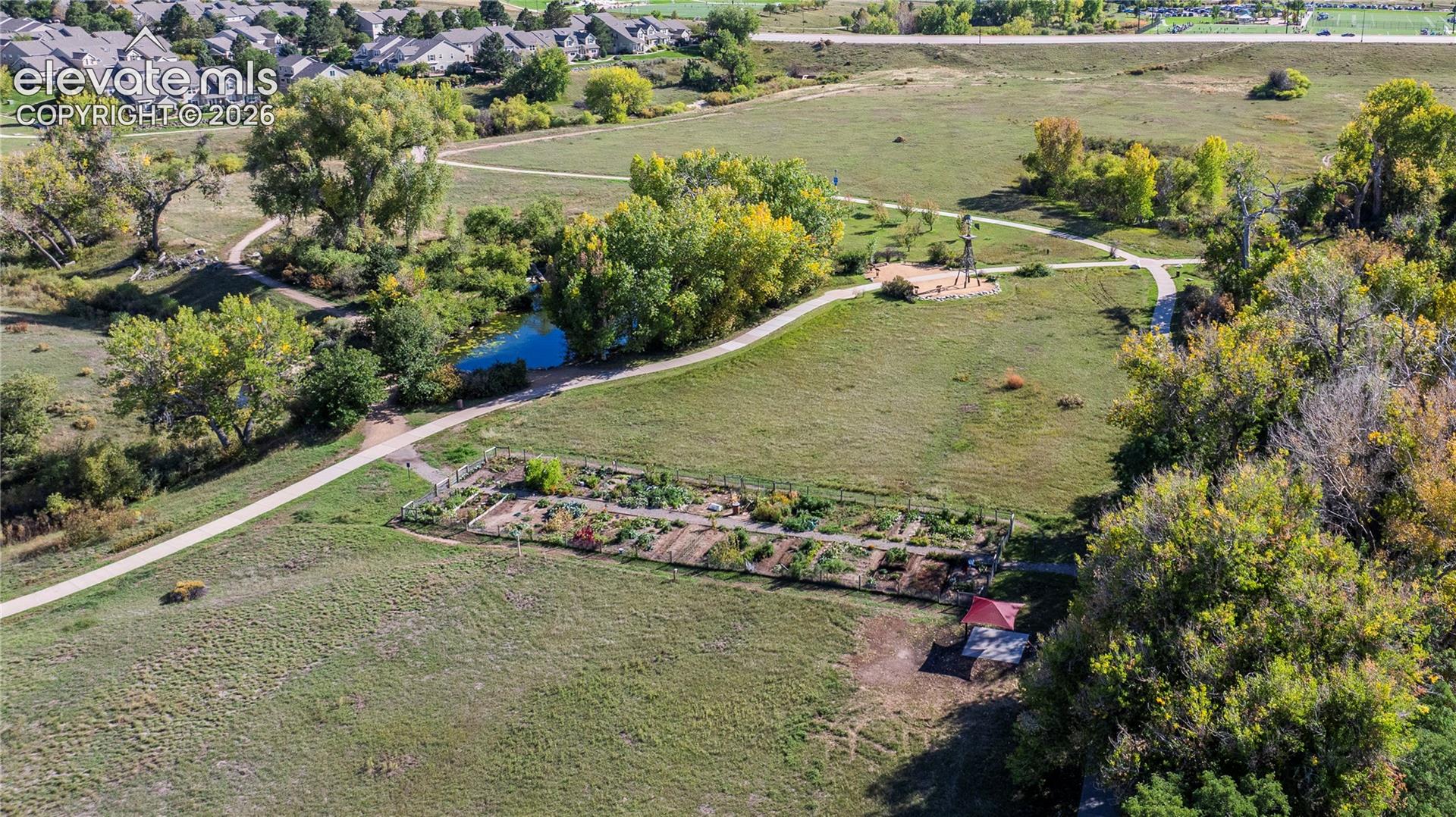 Expansive grounds featuring paved walking paths, a pond, mature trees, a garden area, and a structure with a red roof
