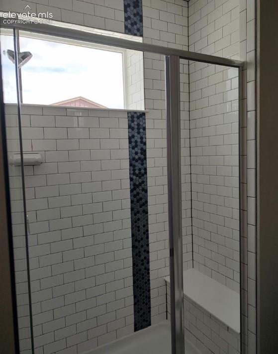 Walk-in shower featuring white subway tile, vertical decorative hexagonal accent tile, integrated built-in bench, and a framed glass enclosure