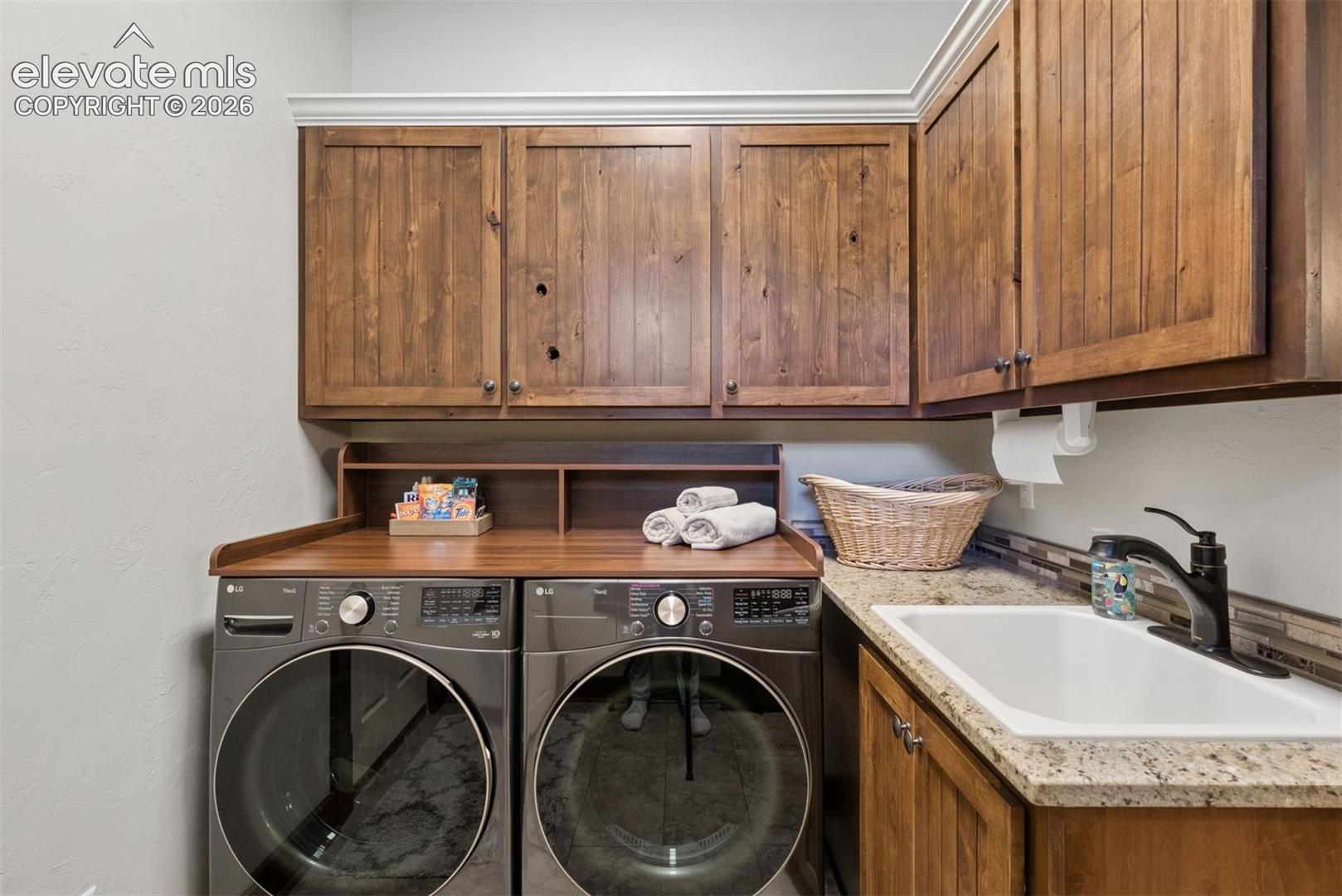 Custom wood-finish cabinetry, stone countertop, drop-in utility sink with matte black faucet, and crown molding