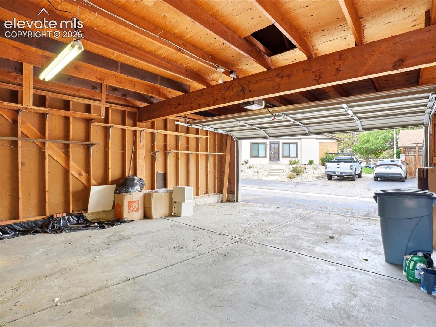 Attached garage featuring exposed timber framing, concrete flooring, and an overhead door mechanism