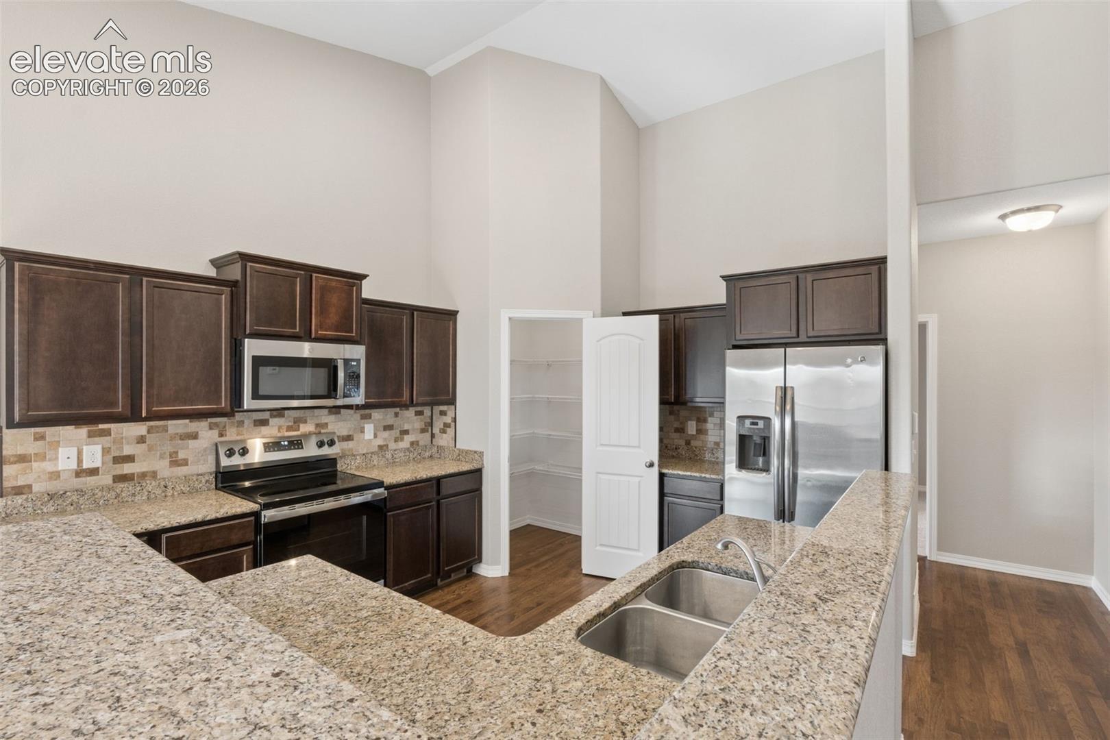 Kitchen featuring a breakfast bar with dual basin stainless steel sink, dark wood cabinetry, stainless steel appliances, and a mosaic tile backsplash