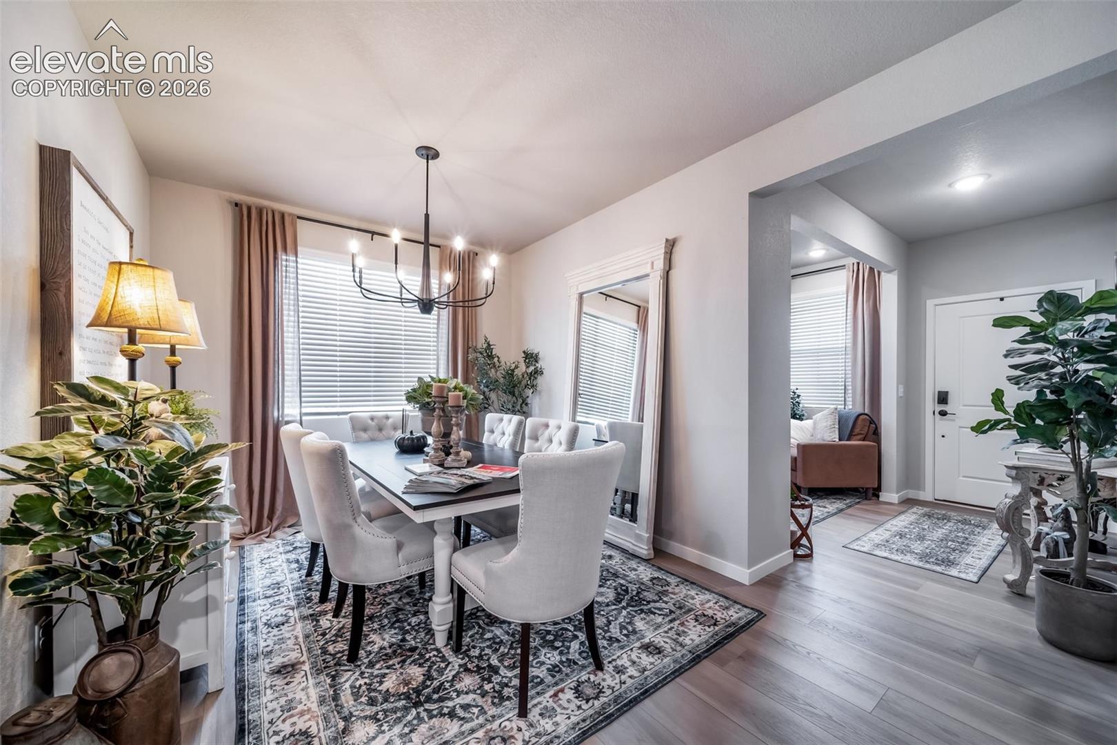 Dining area featuring a contemporary chandelier, wood-finish flooring, white baseboards, and a large window with blinds
*Photos of a model home*