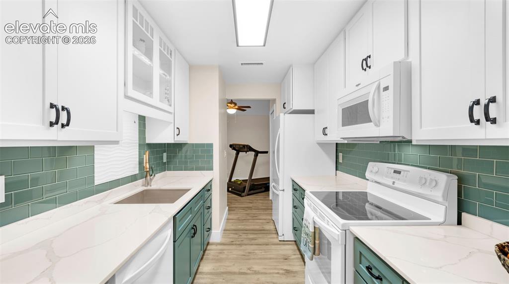 Galley kitchen featuring white upper cabinetry, teal lower cabinetry, light-toned countertops, and a teal subway tile backsplash