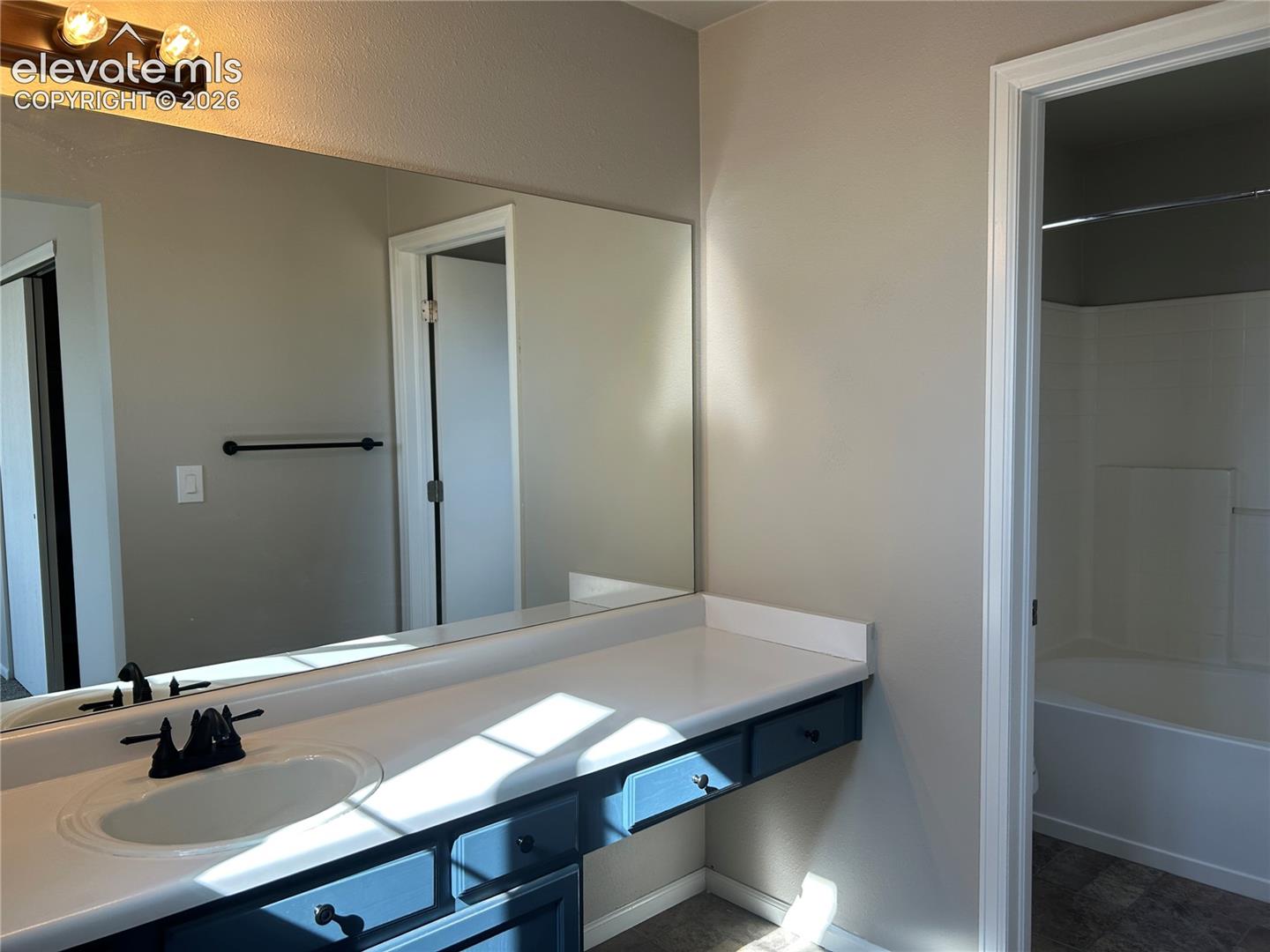 Bathroom vanity featuring a solid surface countertop, an undermount sink with a matte black faucet, painted cabinetry, and a full-width wall mirror with integrated lighting